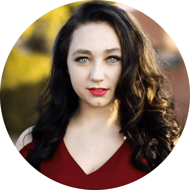 Headshot for Bella Bradbury: red dress, pale skin, dark hair, grey eyes, in an outdoor background