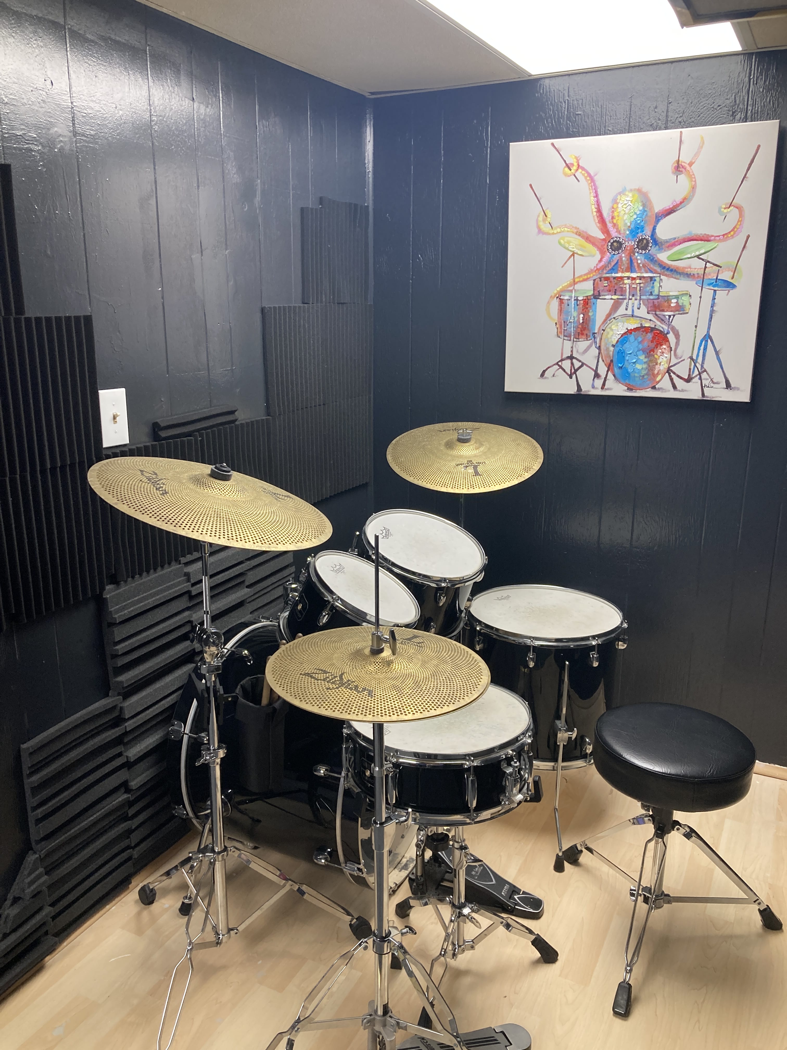 Bass Line Music Studio drum room: black walls with soundproofing, light vinyl floor, octopus playing drums painting, full drum kit