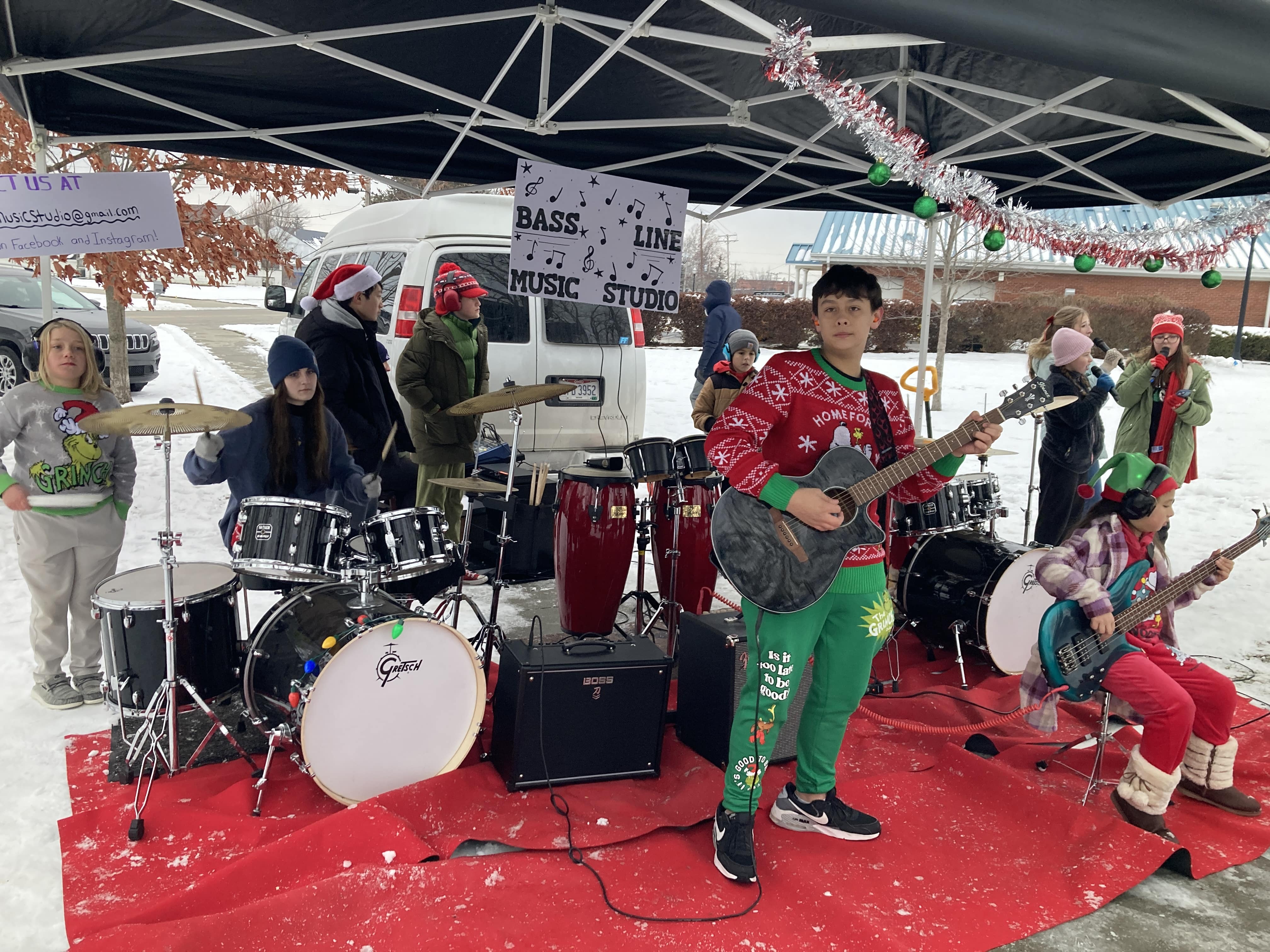 full band setup of holiday event under a tent: instruments included are guitar, 2 drum kits, bass, aux percussion, and singers