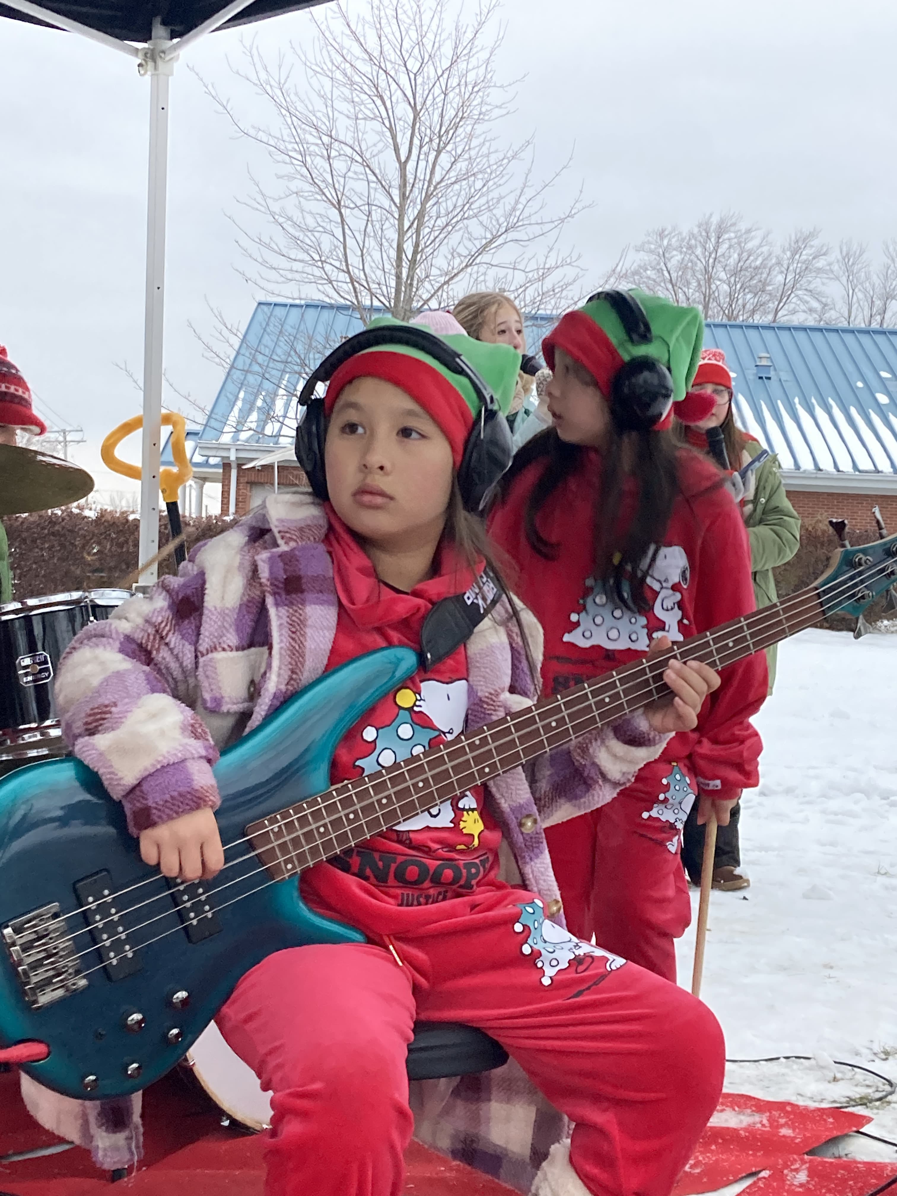 student in a red holiday outfit with hearing protection playing a blue bass at a holiday event