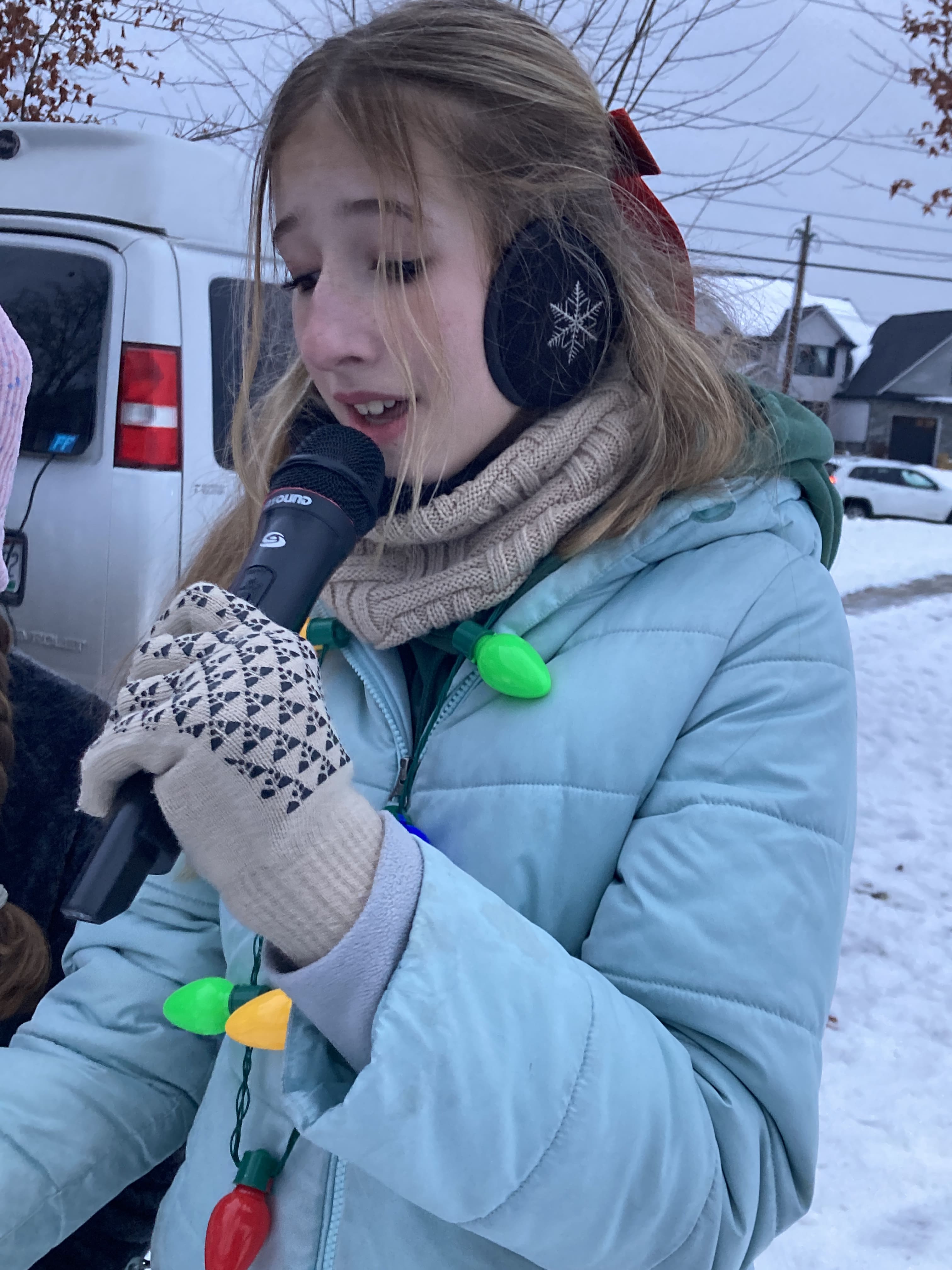 student in a blue jacket singing into a microphone at a holiday event